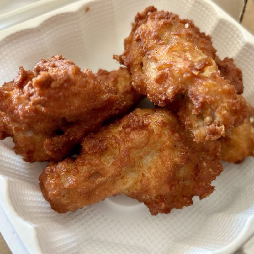 Close-up of several crispy, golden-brown fried chicken pieces in a white takeout container.